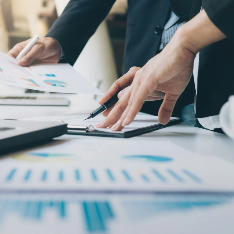 Hands working on documents and charts spread out on a table.