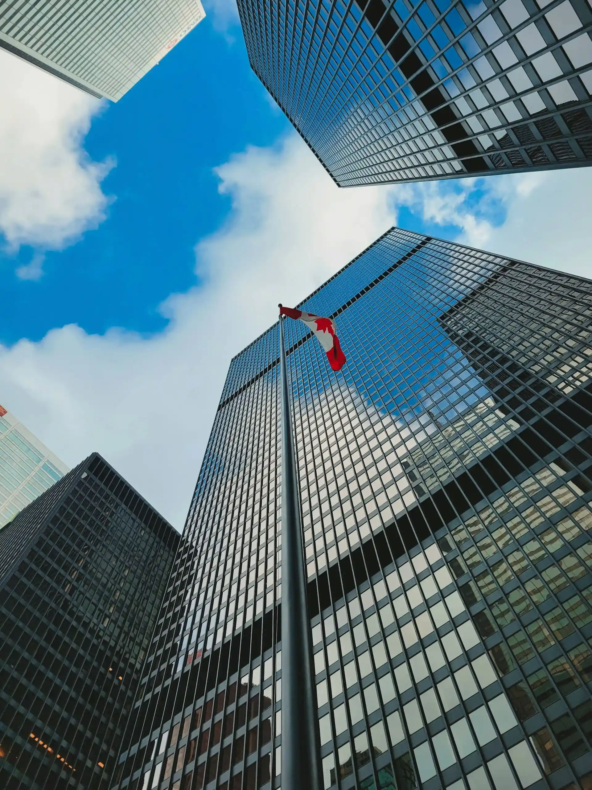 Upward view of modern skyscrapers with the Canadian flag showing in front of the skyscrapers.